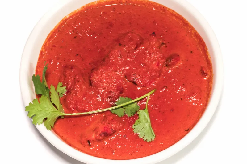 White bowl of deep red curry garnished with cilantro at The Oven