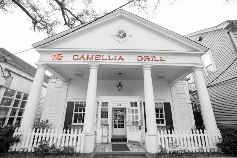 Black-and-white storefront of The Camellia Grill with its red neon sign and white columns in New Orleans
