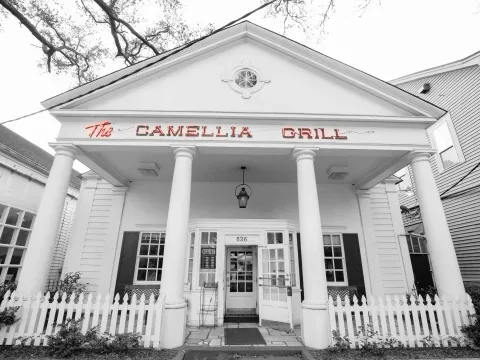 Black-and-white storefront of The Camellia Grill with its red neon sign and white columns in New Orleans