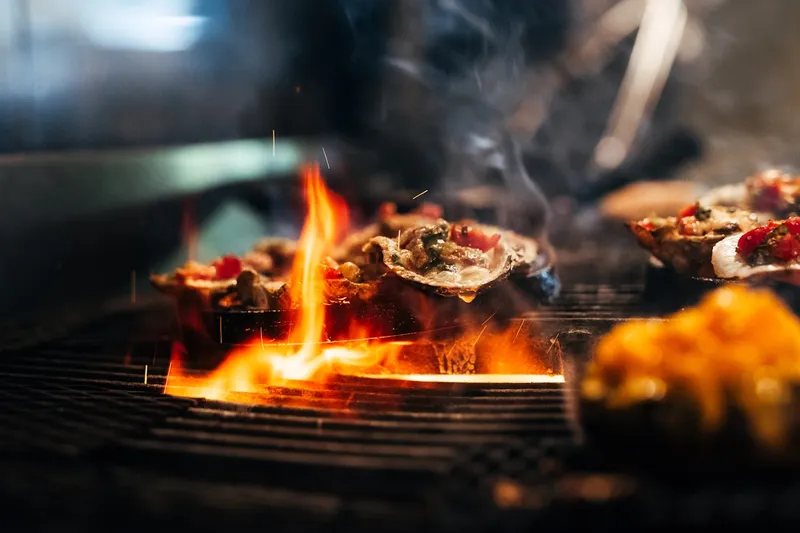 Char-grilled oysters cooking over an open flame at Boathouse Rotisserie & Raw Bar