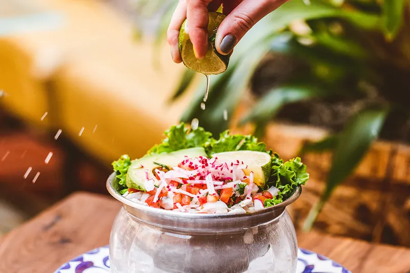 Lime being squeezed over a bowl of ceviche with radish, avocado and tomato at Fonda San Miguel