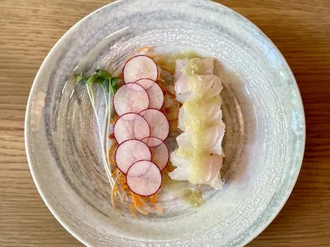 A plate of sashimi-style white fish with thinly sliced radish, microgreens and shaved citrus on a ceramic dish at Takashi in Salt Lake City