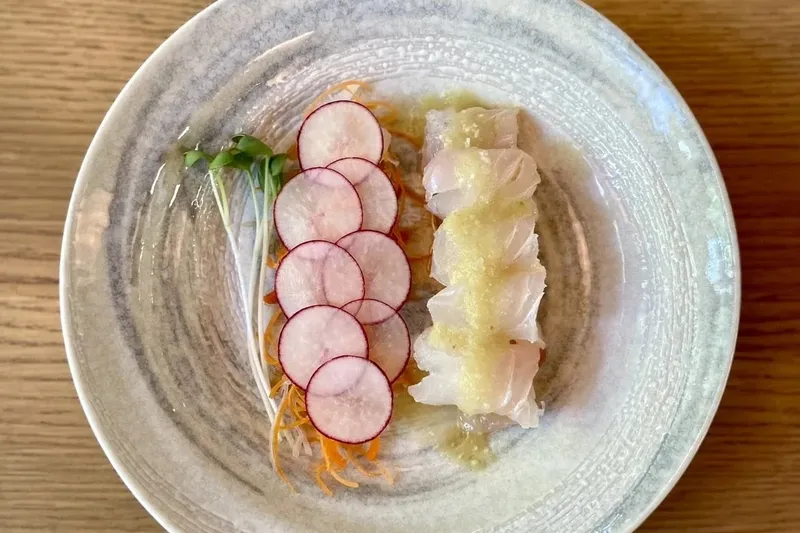 A plate of sashimi-style white fish with thinly sliced radish, microgreens and shaved citrus on a ceramic dish at Takashi in Salt Lake City
