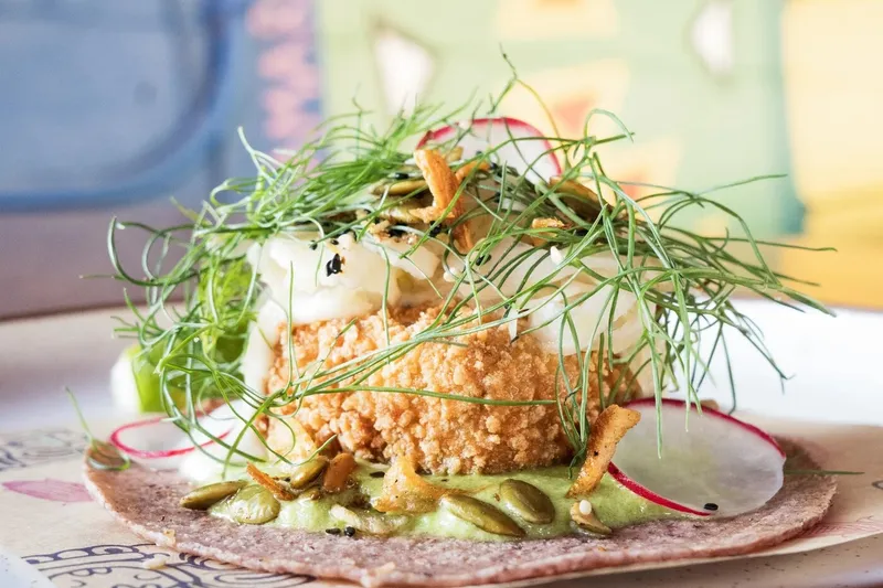 Crisp tostada with greens and radish on a pink corn tortilla at Nixta Taqueria