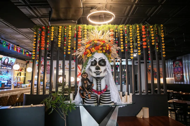 The dining room at Blue Habanero in Richmond, with a large Catrina sculpture in a marigold flower crown beneath hanging garlands