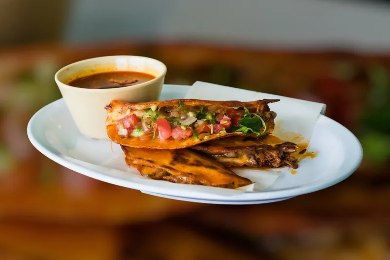 Quesabirria taco with melted cheese and pico de gallo served with a cup of consommé for dipping at Morelia's Taqueria