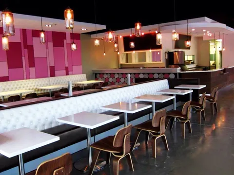 Interior dining room of Cafe 101 in Houston's Bellaire Chinatown, with a pink-tiled accent wall, white tufted booth seating, wood chairs and hanging pendant lights