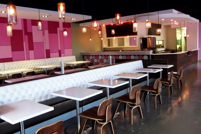 Interior dining room of Cafe 101 in Houston's Bellaire Chinatown, with a pink-tiled accent wall, white tufted booth seating, wood chairs and hanging pendant lights