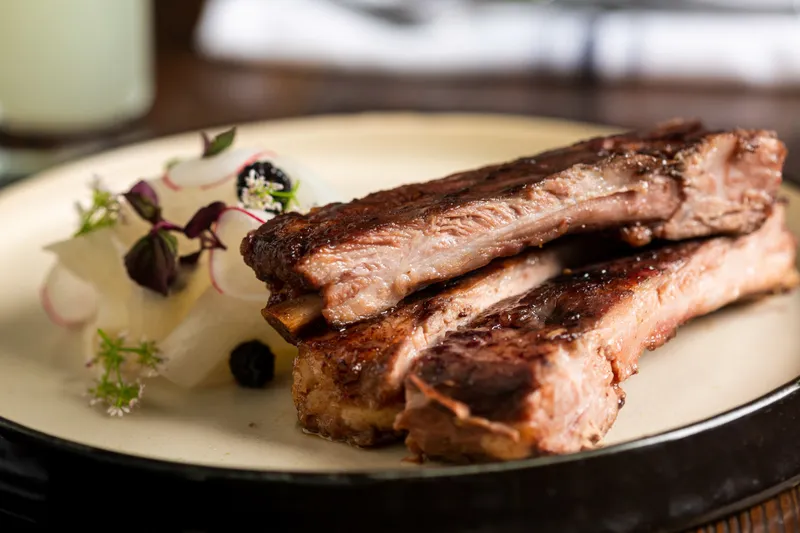 Grilled ribs plated with pickled radish and herbs at Harbinger