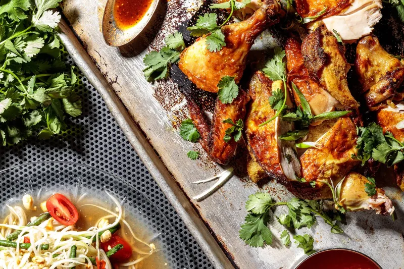 Takoi grilled Thai chicken on a metal tray with cilantro, lime and chili dipping sauces beside a bowl of som tum papaya salad in Detroit