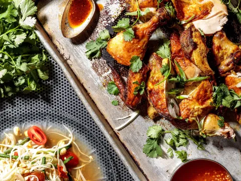 Takoi grilled Thai chicken on a metal tray with cilantro, lime and chili dipping sauces beside a bowl of som tum papaya salad in Detroit