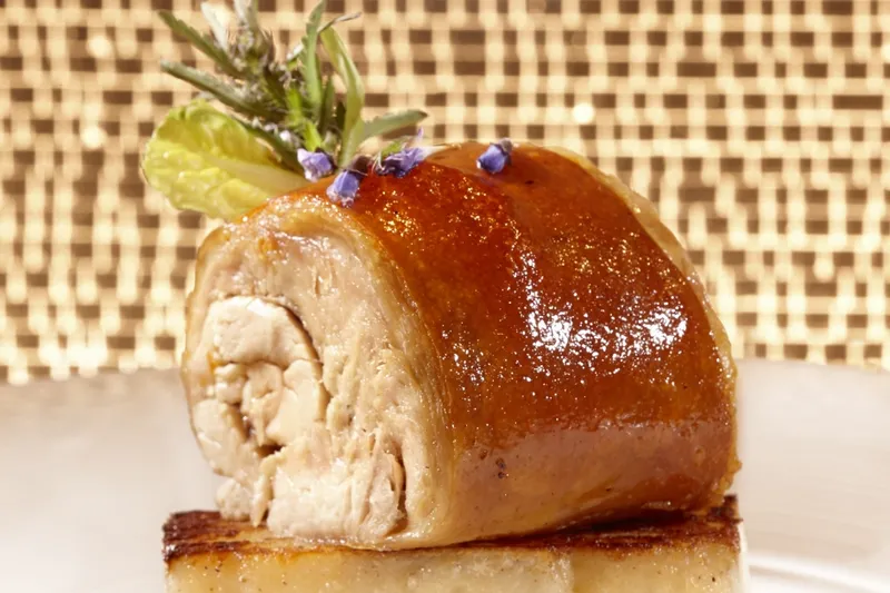 Crisp-skinned roast suckling pig served over a potato cake, garnished with herbs and an edible flower, at Olea in New Haven
