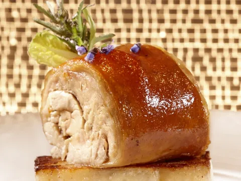 Crisp-skinned roast suckling pig served over a potato cake, garnished with herbs and an edible flower, at Olea in New Haven