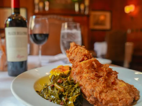 Crispy fried chicken over collard greens and cheddar grits in the candlelit dining room at The Olde Pink House, Savannah