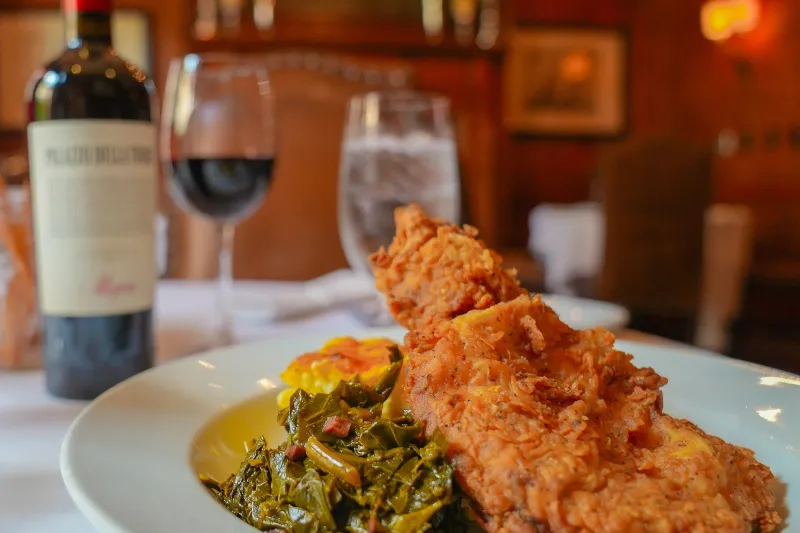 Crispy fried chicken over collard greens and cheddar grits in the candlelit dining room at The Olde Pink House, Savannah