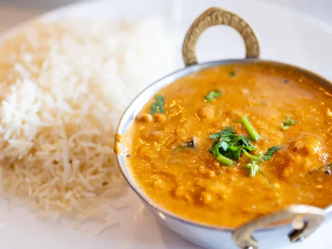 A creamy orange curry served in a small copper karahi beside a mound of basmati rice on a white plate at Rasoi in Pawtucket