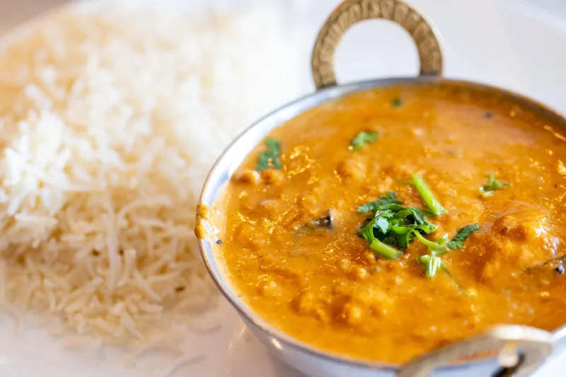 A creamy orange curry served in a small copper karahi beside a mound of basmati rice on a white plate at Rasoi in Pawtucket