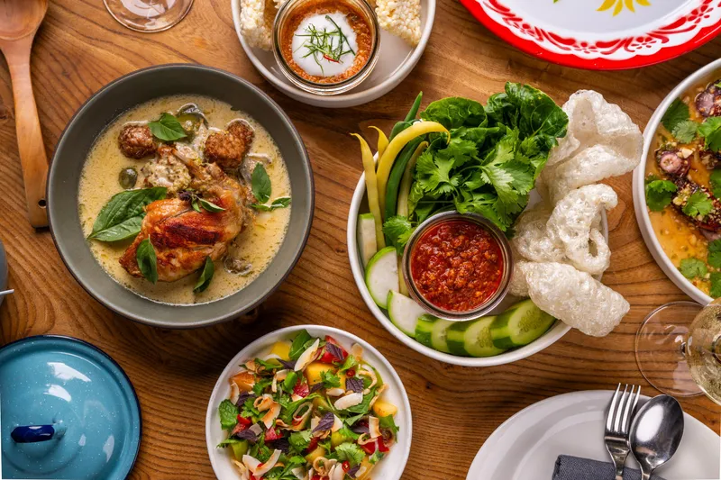 Overhead spread of Thai dishes at Kin Khao including green curry, namprik relish with vegetables, and charred squid