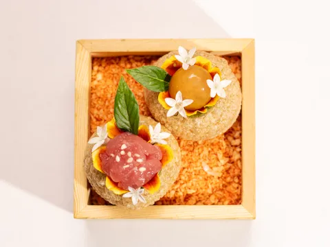 Two crisp pani puri-style bites topped with tuna and a curry pearl, garnished with basil and edible flowers, served in a wooden box at Amrina