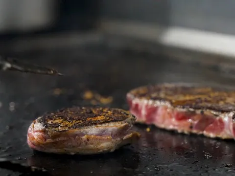 Two hand-cut steaks searing on the flat-top grill at Jess & Jim's Steakhouse