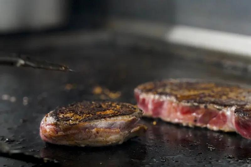 Two hand-cut steaks searing on the flat-top grill at Jess & Jim's Steakhouse