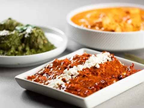 Trio of India Palace curries — a cheese-topped red masala, palak, and a paneer curry in white dishes