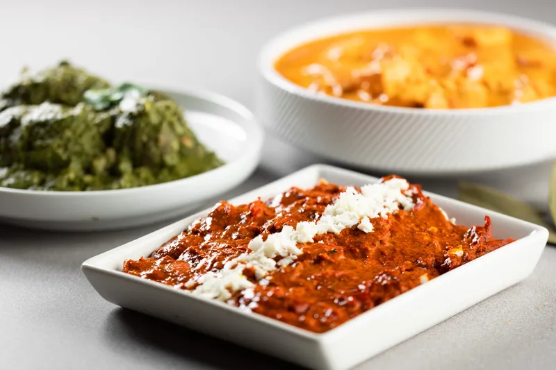 Trio of India Palace curries — a cheese-topped red masala, palak, and a paneer curry in white dishes