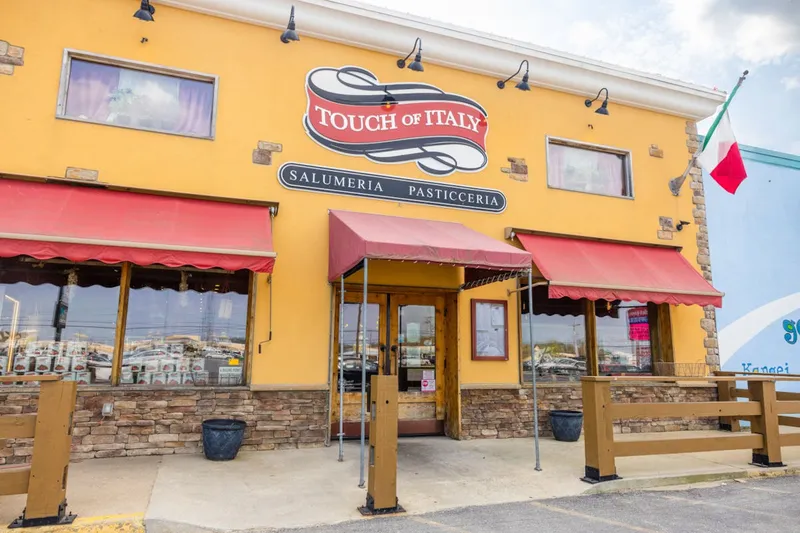 Yellow stucco storefront of Touch of Italy with red awnings over the salumeria and pasticceria windows