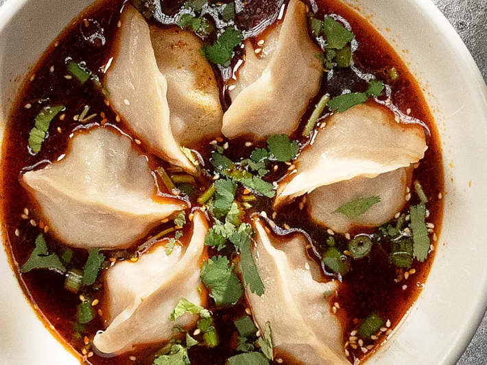 Bowl of The Handpulled Noodle's pork and celery wontons in chili-oil broth topped with cilantro and sesame
