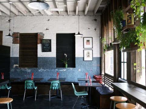 Interior dining room at Xiao Bao Biscuit in Charleston with whitewashed brick walls, teal school chairs, wood counter stools and hanging plants