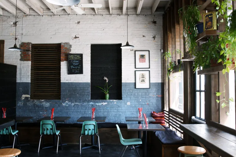Interior dining room at Xiao Bao Biscuit in Charleston with whitewashed brick walls, teal school chairs, wood counter stools and hanging plants