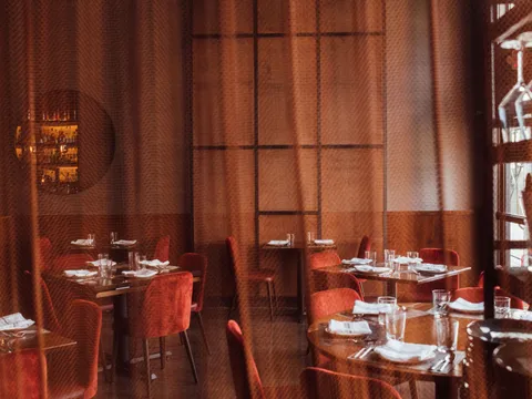 Empty Saffron NOLA dining room with copper-toned walls, red chairs, and set tables
