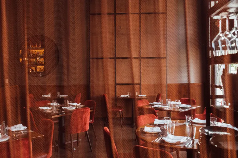 Empty Saffron NOLA dining room with copper-toned walls, red chairs, and set tables