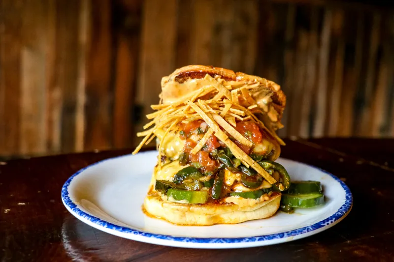 A grilled specialty sandwich topped with peppers, salsa and crispy tortilla strips on a blue-rimmed plate at Dinosaur Bar-B-Que in Syracuse