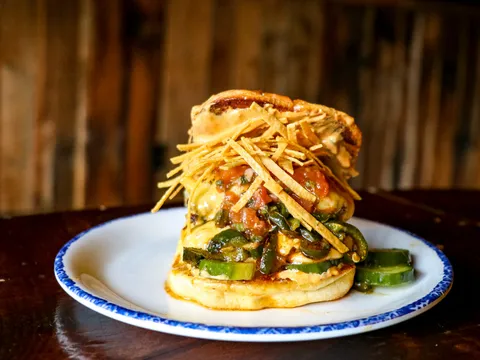 A grilled specialty sandwich topped with peppers, salsa and crispy tortilla strips on a blue-rimmed plate at Dinosaur Bar-B-Que in Syracuse