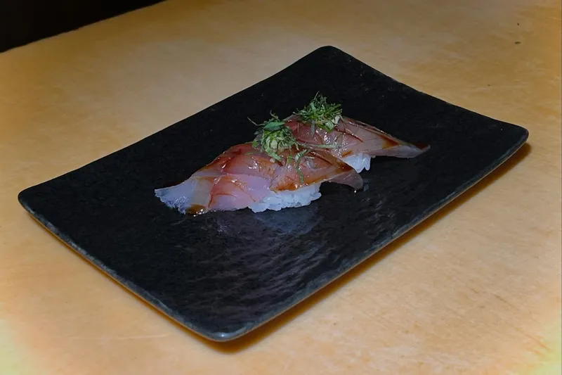Nigiri topped with cured fish and shiso on a black rectangular plate at Sushi Note, from the restaurant's website