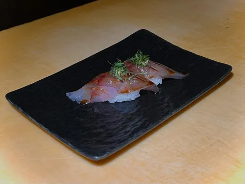 Nigiri topped with cured fish and shiso on a black rectangular plate at Sushi Note, from the restaurant's website