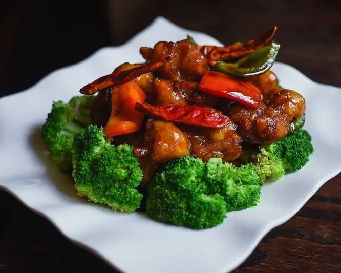 General Tso's chicken with dried chilies and bell peppers ringed by steamed broccoli on a white plate at Lee How Fook in Philadelphia