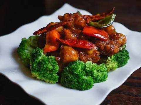 General Tso's chicken with dried chilies and bell peppers ringed by steamed broccoli on a white plate at Lee How Fook in Philadelphia