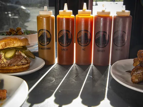 Slows Bar BQ house barbecue sauces in branded squeeze bottles beside a pulled pork sandwich, salad and smoked wings in Detroit