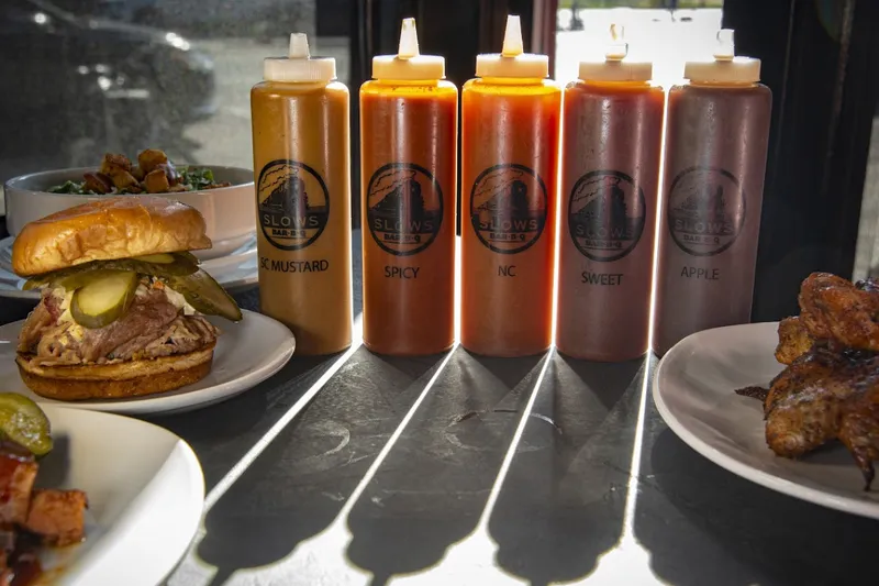 Slows Bar BQ house barbecue sauces in branded squeeze bottles beside a pulled pork sandwich, salad and smoked wings in Detroit