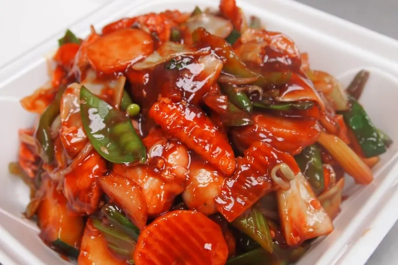 Sweet-and-sour chicken with vegetables in a white takeout container at Three Happiness Express.