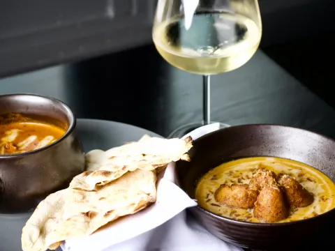 Butter chicken and malai kofta in copper bowls with naan and a glass of white wine at Bhatti Indian Grill