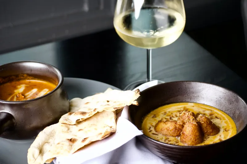 Butter chicken and malai kofta in copper bowls with naan and a glass of white wine at Bhatti Indian Grill
