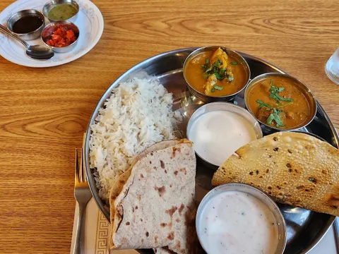 Thali at Shalimar of India in Burlington — a steel platter of basmati rice, two curries, raita, chapati and papad, with a side plate of chutneys, on a wood table