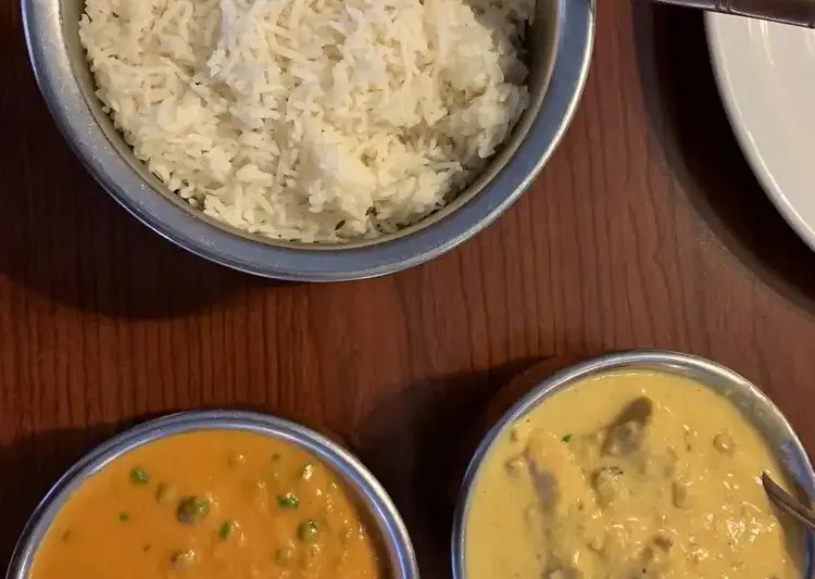 Two curries with peas and basmati rice in steel bowls on a wooden table at Namaste Shangri-La in Anchorage