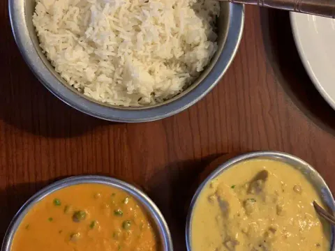 Two curries with peas and basmati rice in steel bowls on a wooden table at Namaste Shangri-La in Anchorage