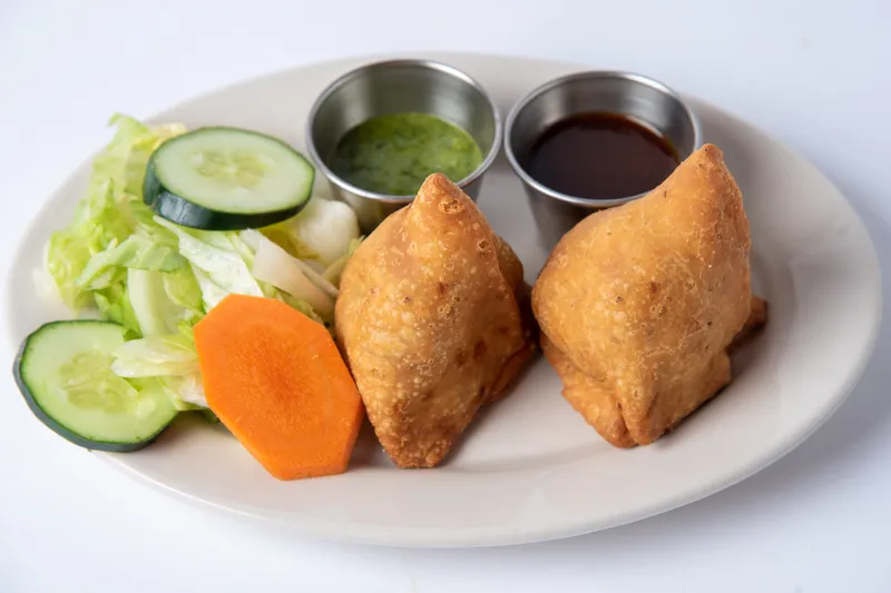 Two vegetable samosas served with salad, green chutney, and tamarind sauce at Namaste Baltimore