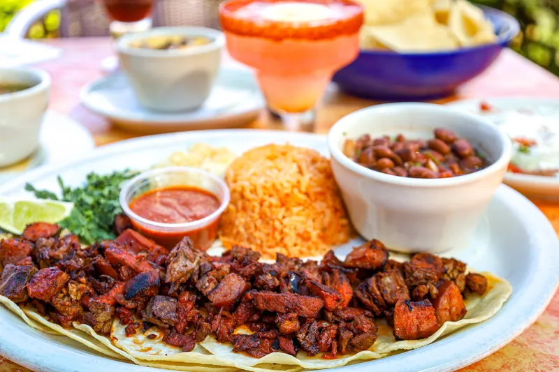 Plate of grilled tacos with Mexican rice and charro beans beside a margarita and chips at Aldaco's Mexican Cuisine