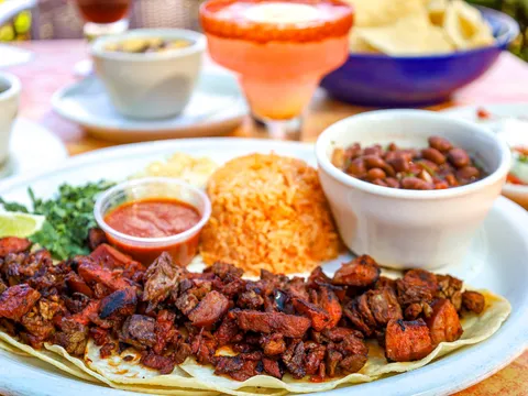 Plate of grilled tacos with Mexican rice and charro beans beside a margarita and chips at Aldaco's Mexican Cuisine